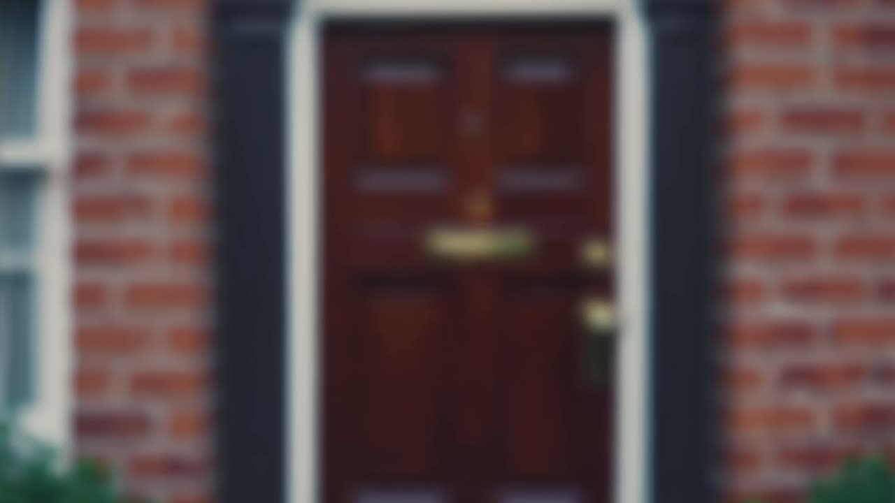 Close-up video of a classic wooden door with brass fixtures, framed by red brick