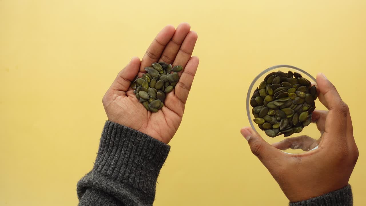 Hands holding and pouring pumpkin seeds from a glass bowl