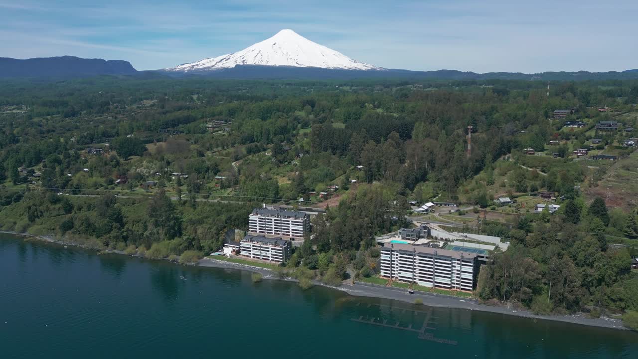 Ascending Drone Shot Over Lake and Modern Waterfront Buildings with Snow-Capped Villarrica Volcano in the Background Surrounded by Lush Forest