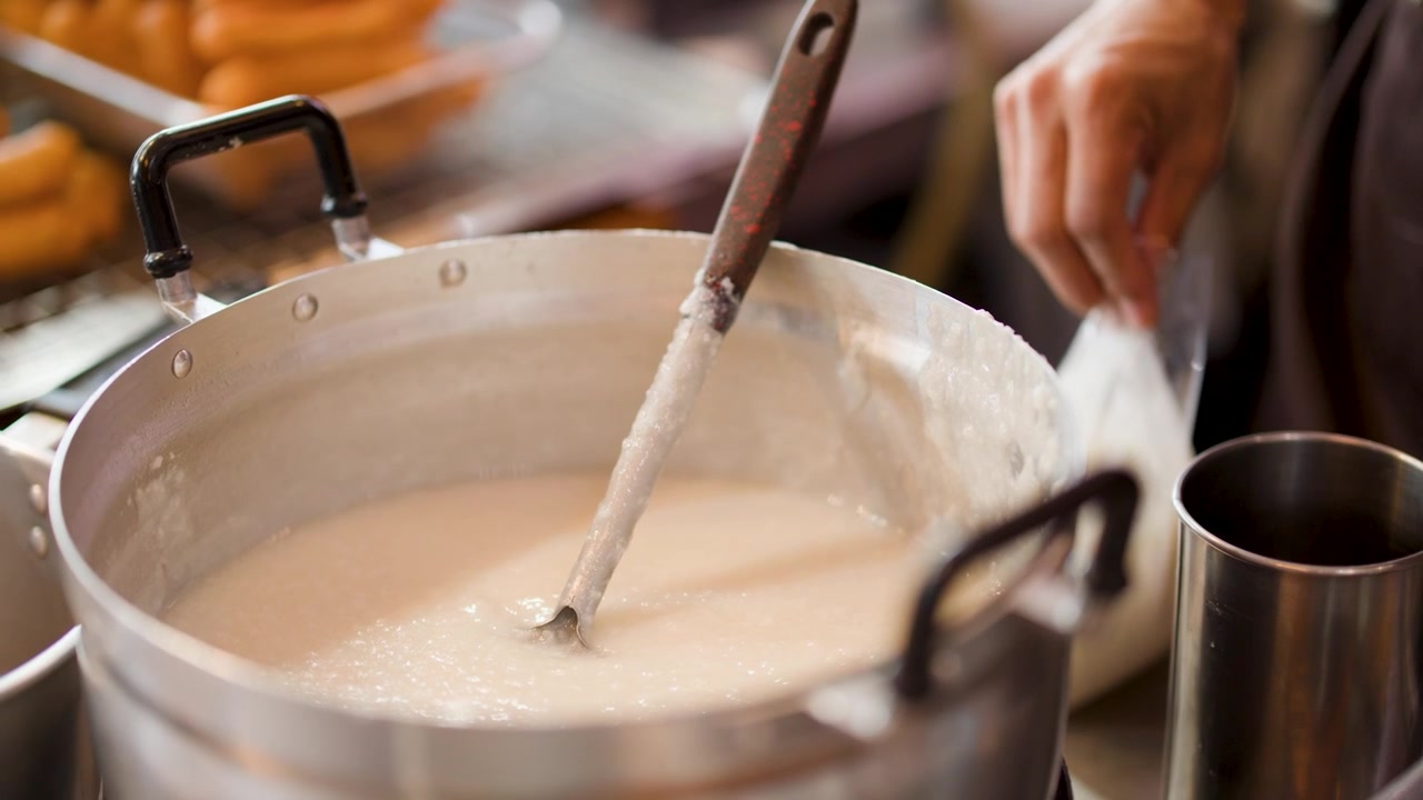Gros plan d'un vendeur préparant du congee traditionnel dans une grande marmite sur un marché