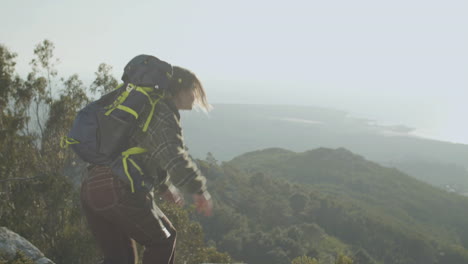 vista trasera de una excursionista parada en la cima de la montaña con las manos arriba y disfrutando de la vista 1