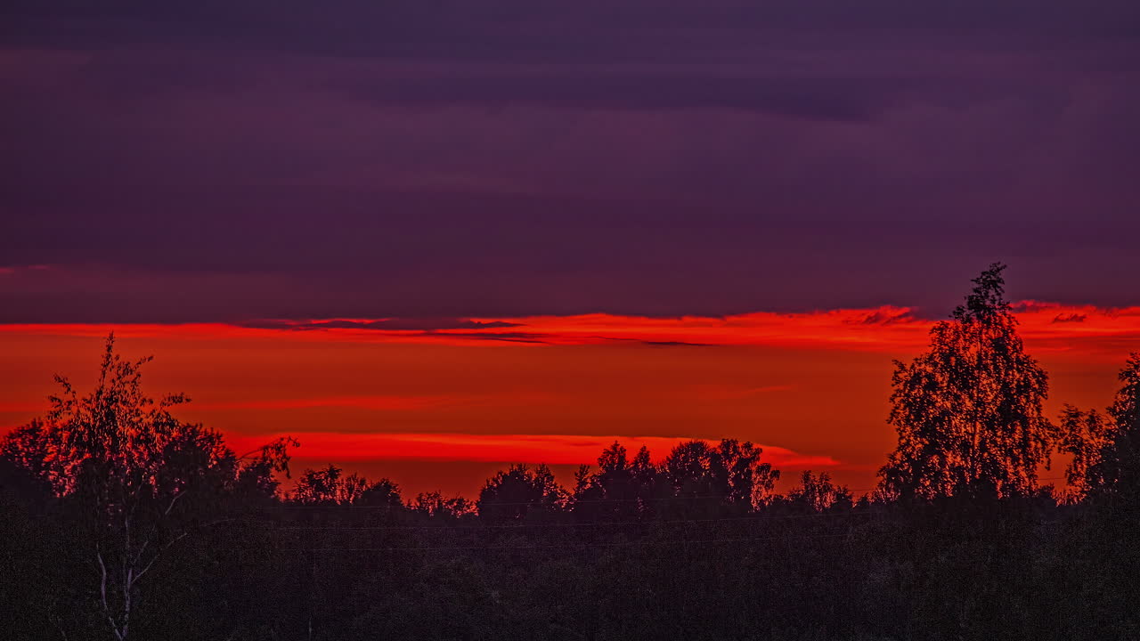 Zeitraffer eines rötlichen, bewölkten Sonnenuntergangs über einer bewachsenen Landschaft.