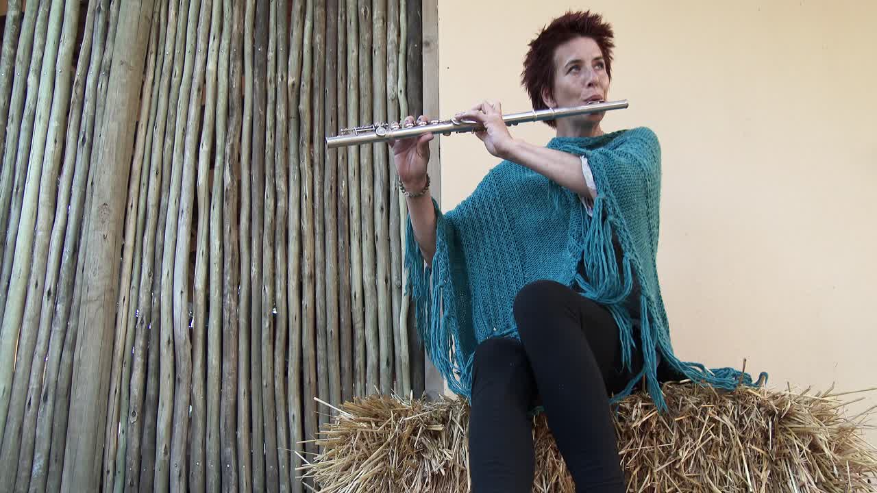 una joven música toca una flauta mientras se sienta en un fardo de paja