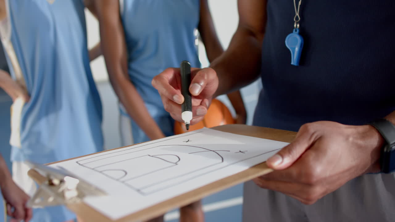 Coach drawing basketball play on clipboard, instructing players on court strategy