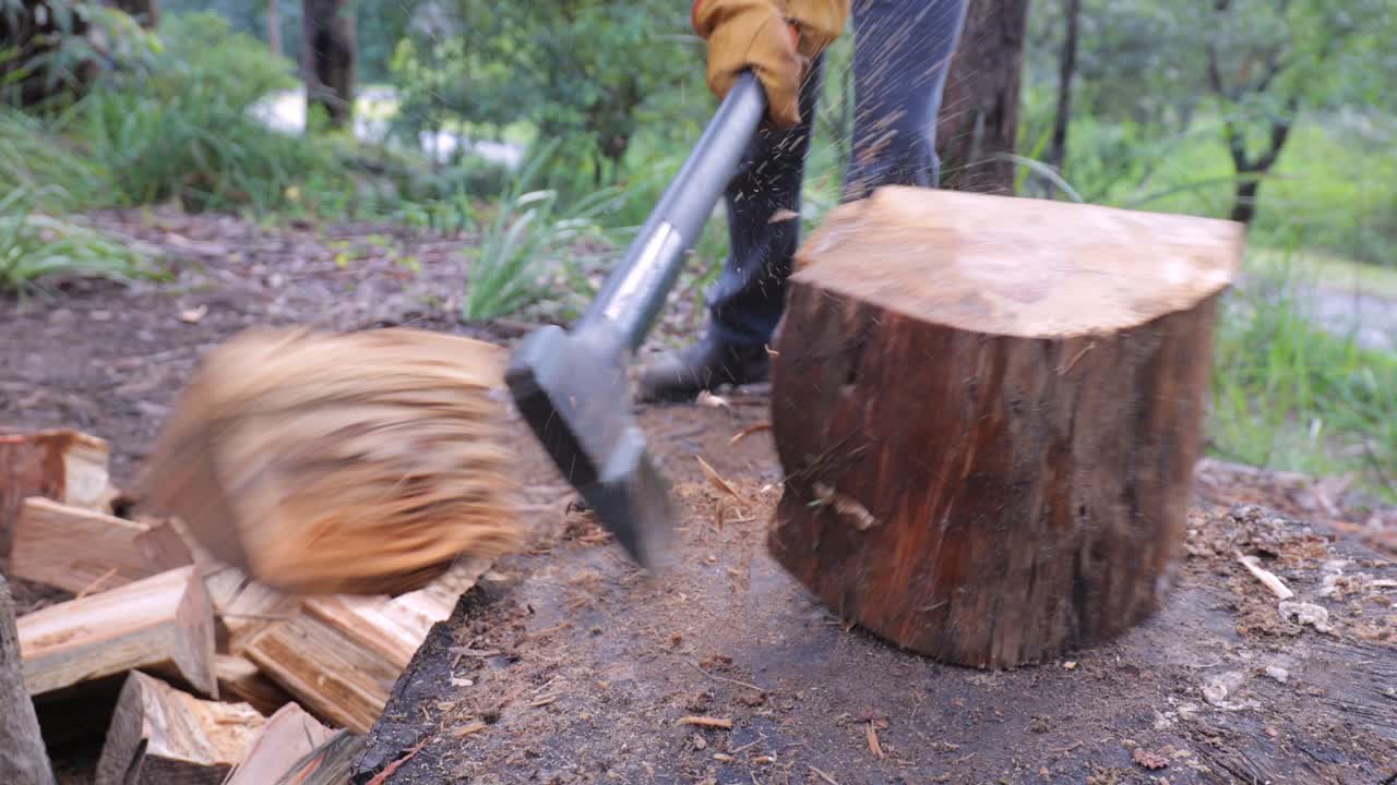겨울 연료 - 도끼, 통나무, 직장에 있는 사람, 다리, 작업 부츠, 작업 장갑 - 남자가 도끼로 통나무를 쪼갤 때 뒤에 있는 시골 자연 숲지대 - 4k