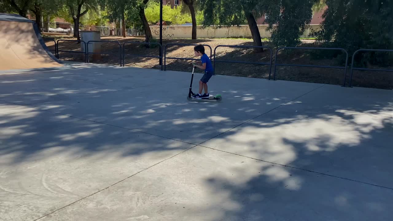 Five year old boy skating with a scooter in a skate park