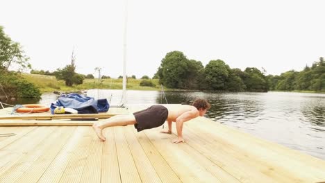 young man does planche-pushups on jetty by river