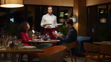 Waiter-serving-hungry-couple-in-fancy-restaurant.-Man-putting-plates-on-table.