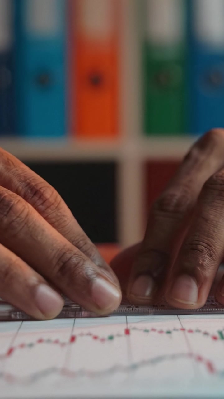 Close-up on Hands Using a Ruler to Analyze Graphs and Data Trends, Surrounded by Colorful Folders in a Well-Organized Workspace Focused on Precision and Analysis