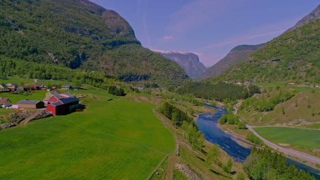 aerial drone forward moving shot over village houses on lush valley in mountainous landscape with river flowing through in aurland, norway at daytime