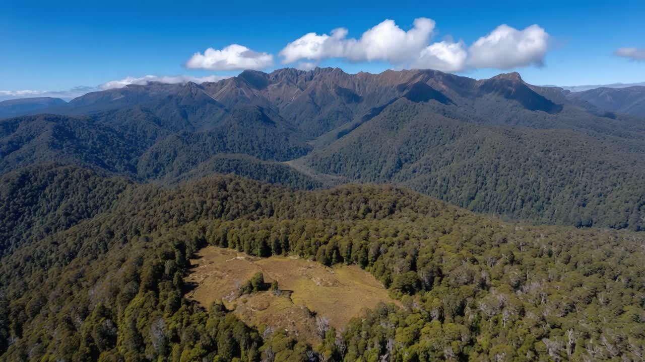 Stunning Aerial View of Majestic Mountain Range Surrounded by Lush Green Forests Under a Bright Blue Sky with Fluffy White Clouds