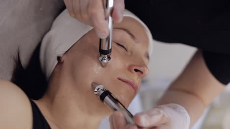 beautician doctor makes woman micro currents face therapy using electrical impulses in spa salon